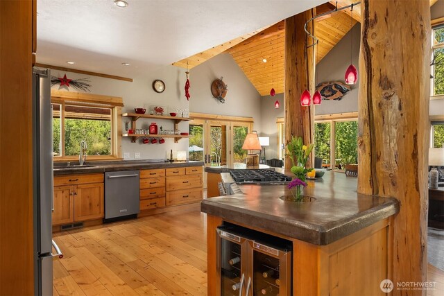 kitchen with appliances with stainless steel finishes, beverage cooler, dark countertops, a sink, and plenty of natural light