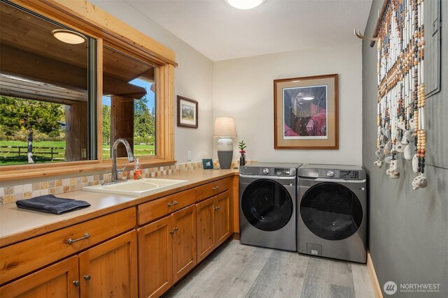 washroom with washing machine and clothes dryer, light wood-style floors, and cabinet space