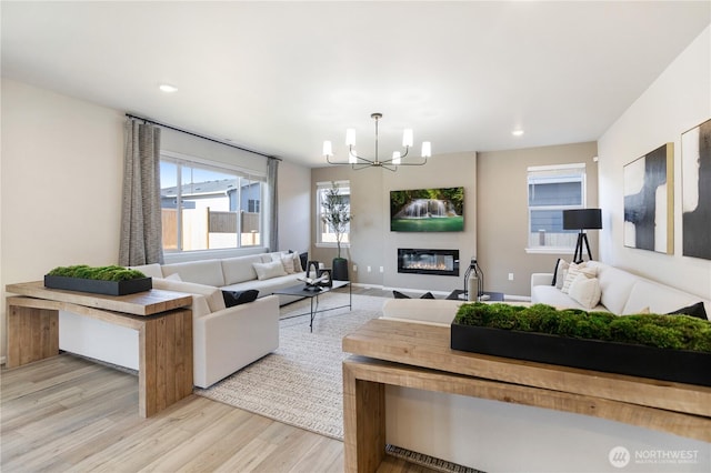 living area featuring a chandelier, light wood-style flooring, recessed lighting, and a glass covered fireplace