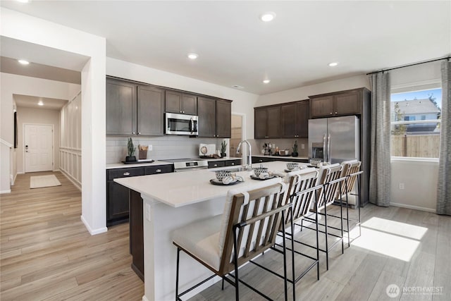 kitchen with appliances with stainless steel finishes, dark brown cabinets, light wood-type flooring, a kitchen bar, and light countertops