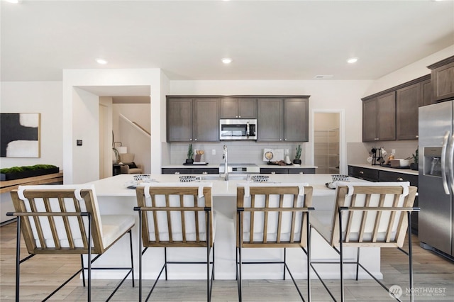 kitchen featuring stainless steel appliances, a sink, light countertops, dark brown cabinets, and backsplash