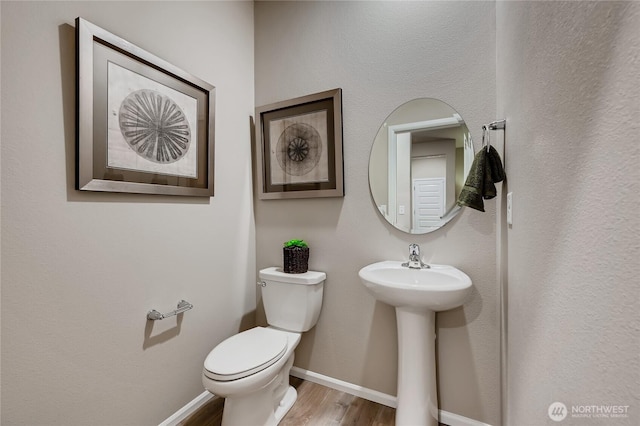 bathroom featuring wood finished floors, toilet, baseboards, and a sink