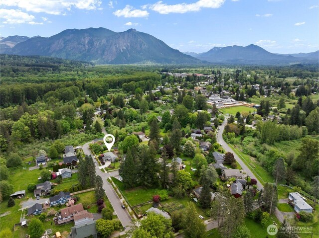 aerial view of property and surrounding area featuring a mountainous background, a heavily wooded area, and nearby suburban area