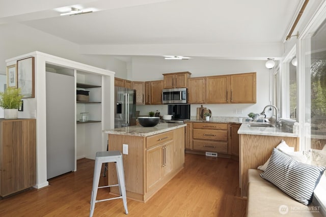kitchen with appliances with stainless steel finishes, a sink, lofted ceiling, light wood-style flooring, and a center island
