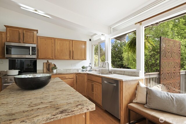 kitchen with appliances with stainless steel finishes, a sink, lofted ceiling, light stone counters, and light wood finished floors