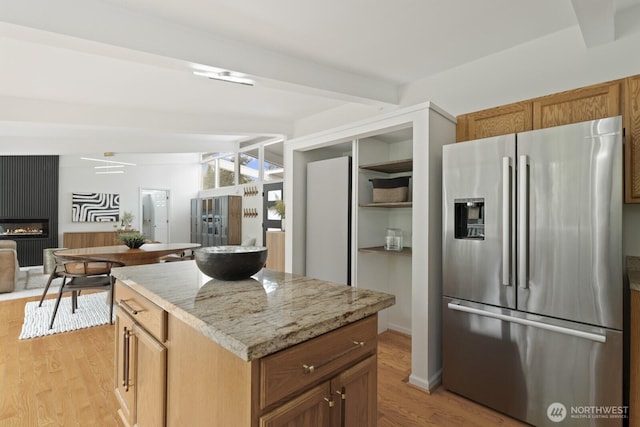 kitchen with stainless steel fridge with ice dispenser, light wood-style floors, beamed ceiling, a kitchen island, and light stone countertops