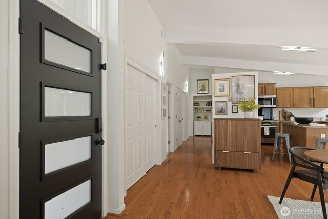 kitchen with appliances with stainless steel finishes, brown cabinets, wood finished floors, and a kitchen island
