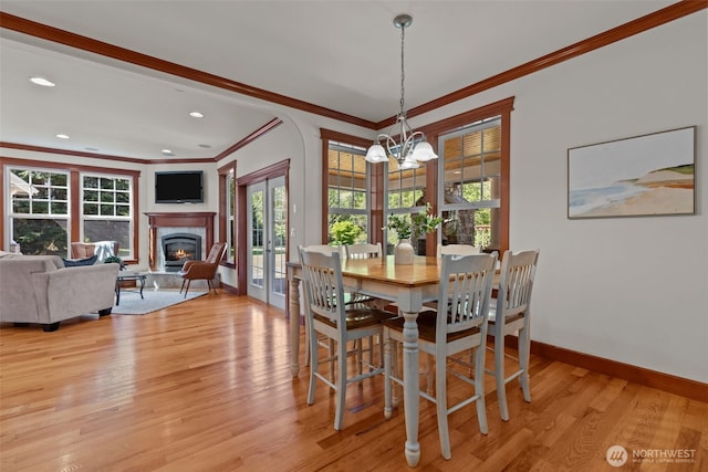 13514 95th Ave NE, Arlington, WA 98223 - dining area featuring crown molding, a chandelier, a glass covered fireplace, baseboards, and light wood-style flooring