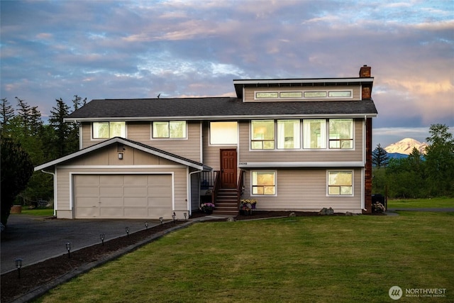 split foyer home featuring a chimney, asphalt driveway, a lawn, and a garage
