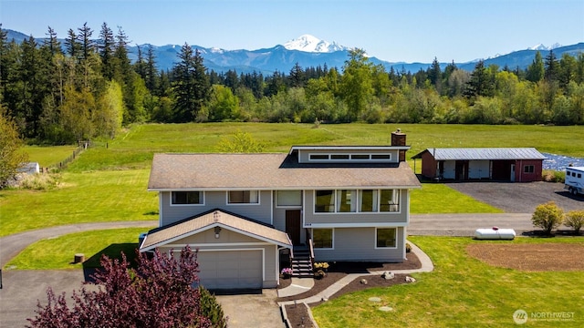 view of front of home featuring a chimney, a mountain view, a garage, driveway, and a front lawn