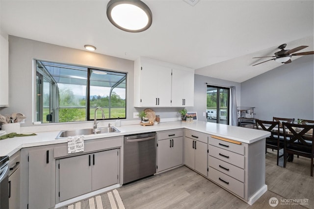 kitchen featuring stainless steel dishwasher, a sink, a peninsula, light wood-type flooring, and light countertops