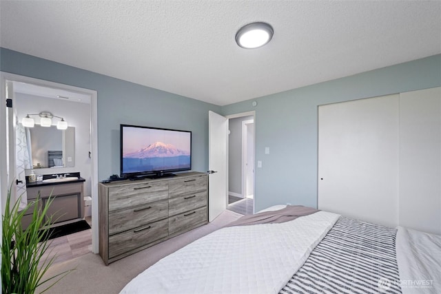 bedroom with a closet, light carpet, a sink, and a textured ceiling
