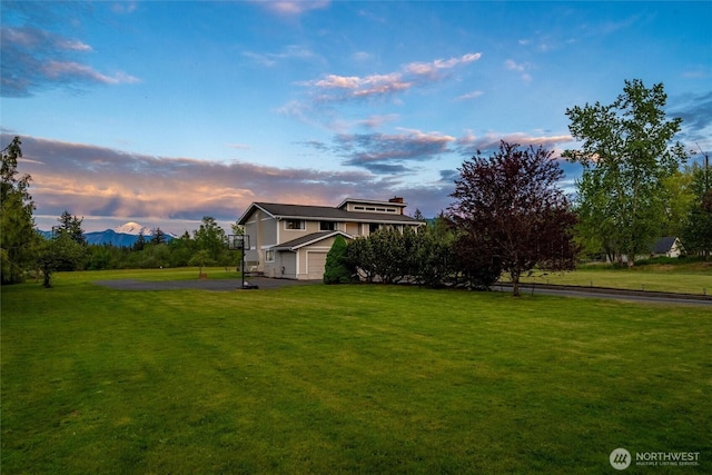 yard at dusk with asphalt driveway, a yard, and an attached garage