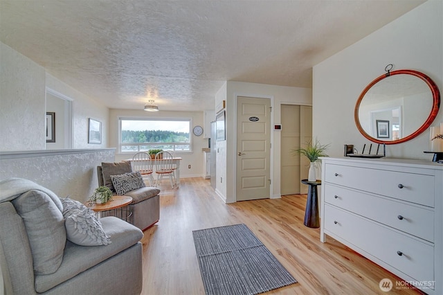living room featuring light wood-type flooring, a textured ceiling, and baseboards