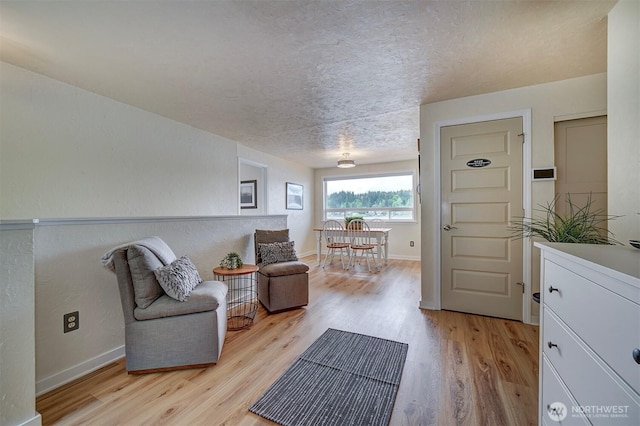 living area with light wood-type flooring, a textured ceiling, and baseboards