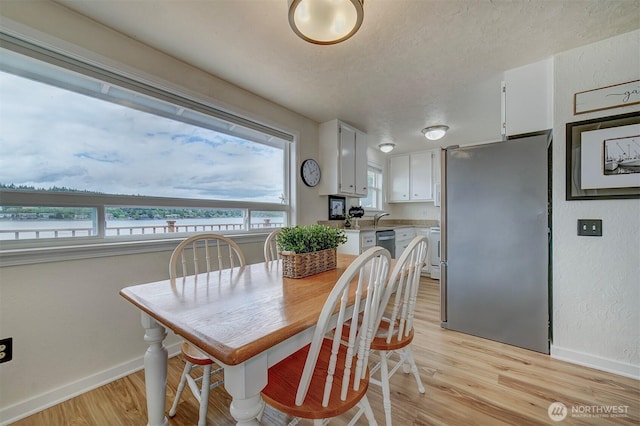 dining room featuring light wood-style flooring, baseboards, and a textured ceiling