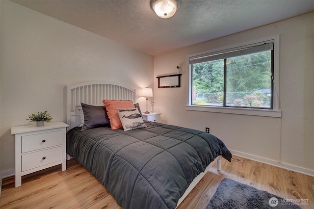 bedroom featuring light wood-style flooring, baseboards, and a textured ceiling