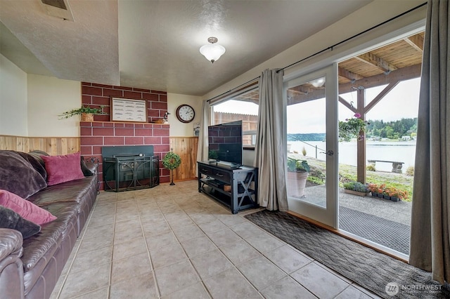 living area featuring wooden walls, a wainscoted wall, healthy amount of natural light, a tiled fireplace, and light tile patterned flooring