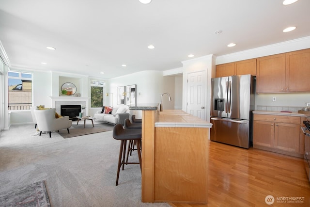kitchen featuring stainless steel refrigerator with ice dispenser, tile counters, a breakfast bar, a sink, and recessed lighting