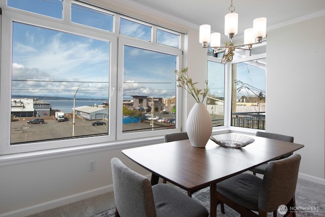 carpeted dining room with a chandelier, baseboards, crown molding, and a water view