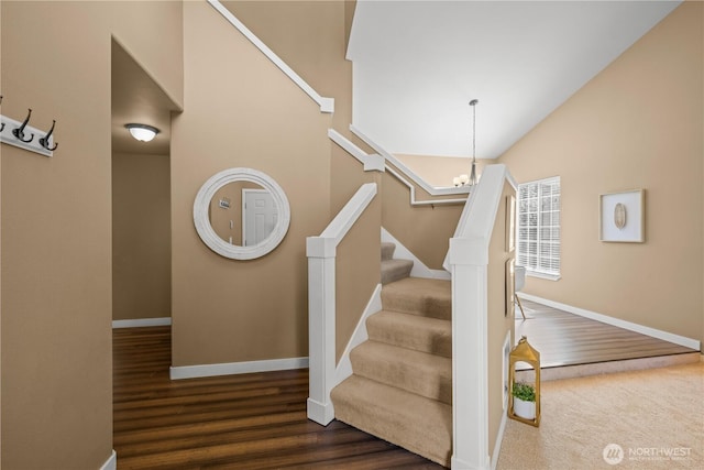 staircase with baseboards, wood finished floors, a chandelier, and high vaulted ceiling
