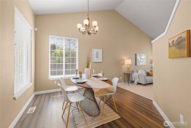 dining area with a chandelier, plenty of natural light, baseboards, wood finished floors, and high vaulted ceiling