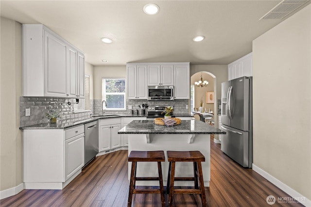 kitchen featuring appliances with stainless steel finishes, white cabinetry, a chandelier, dark wood-type flooring, and a kitchen island