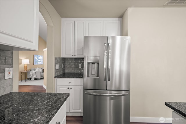 kitchen featuring stainless steel refrigerator with ice dispenser, white cabinets, dark stone countertops, and decorative backsplash