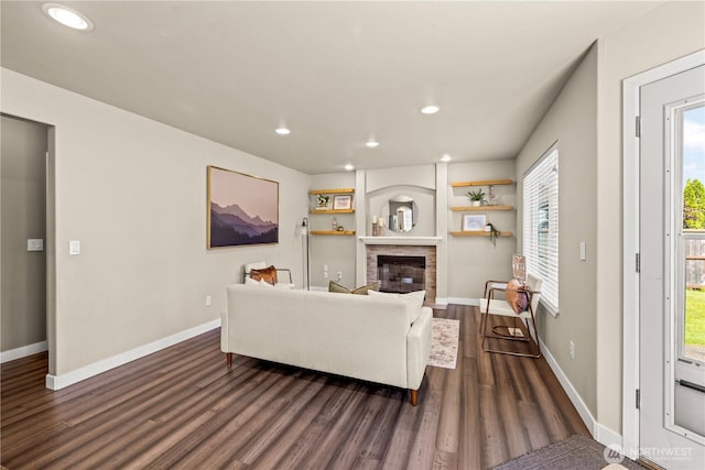 living room featuring dark wood-type flooring, recessed lighting, baseboards, and a glass covered fireplace