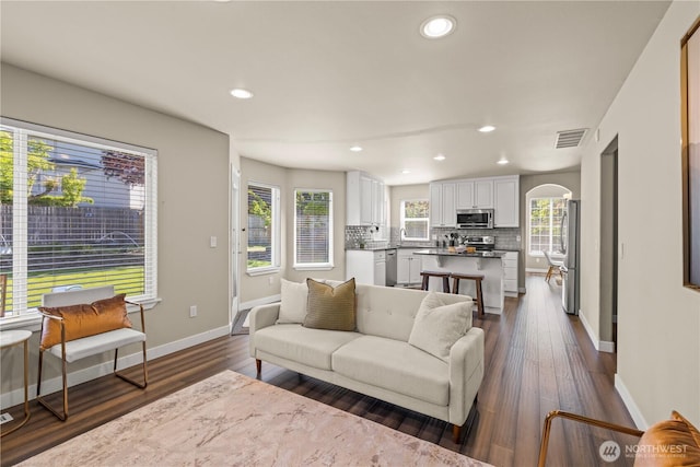 living room with arched walkways, baseboards, recessed lighting, and dark wood-type flooring
