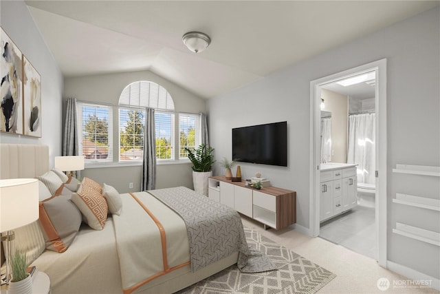 bedroom featuring lofted ceiling, light colored carpet, and ensuite bath