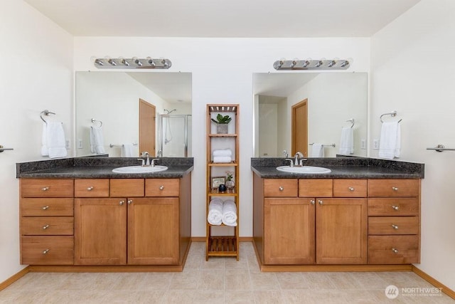 full bath featuring two vanities, a stall shower, and baseboards