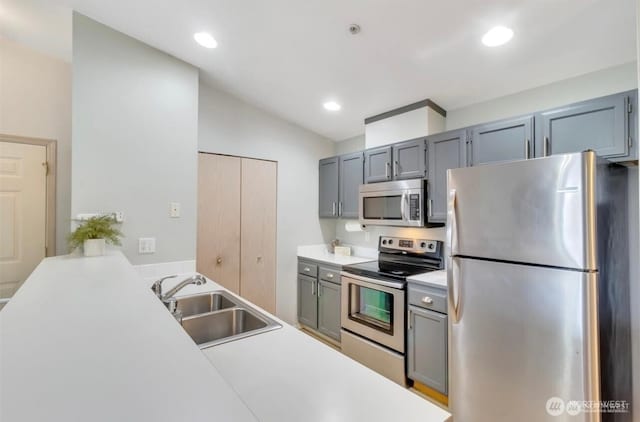 kitchen featuring appliances with stainless steel finishes, a sink, vaulted ceiling, light countertops, and gray cabinets