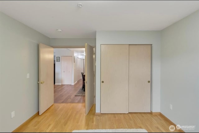 unfurnished bedroom featuring light wood-style flooring, a closet, and baseboards