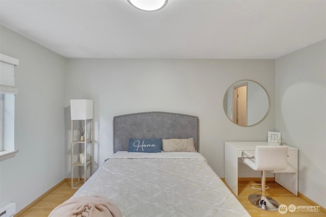 bedroom with wood finished floors, a baseboard radiator, and baseboards