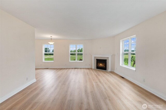 unfurnished living room featuring light wood-type flooring, a fireplace with flush hearth, and baseboards