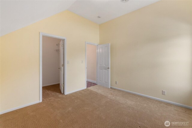 unfurnished bedroom featuring a spacious closet, carpet flooring, lofted ceiling, baseboards, and a closet