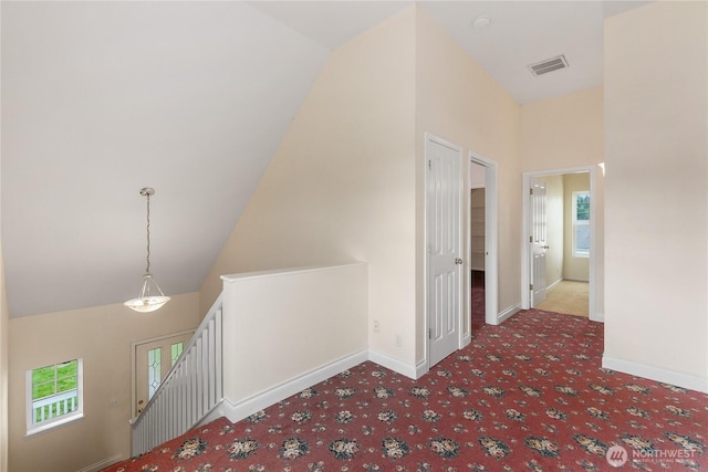 corridor with an upstairs landing, plenty of natural light, baseboards, and high vaulted ceiling