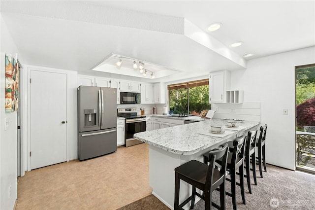 kitchen with stainless steel appliances, a peninsula, white cabinetry, healthy amount of natural light, and recessed lighting