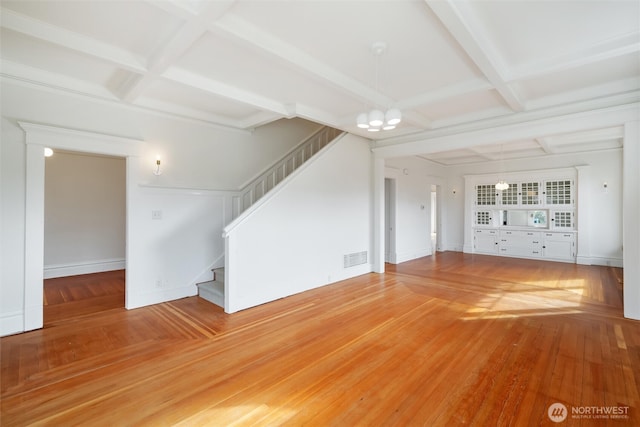 unfurnished living room with coffered ceiling, stairs, a chandelier, beamed ceiling, and wood finished floors
