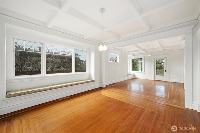 empty room featuring coffered ceiling, beam ceiling, baseboards, and wood finished floors