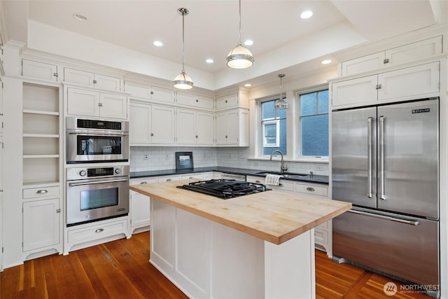 kitchen featuring appliances with stainless steel finishes, butcher block counters, a sink, dark wood-style floors, and recessed lighting