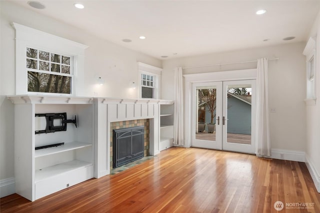 unfurnished living room featuring wood finished floors, a fireplace with flush hearth, recessed lighting, french doors, and baseboards