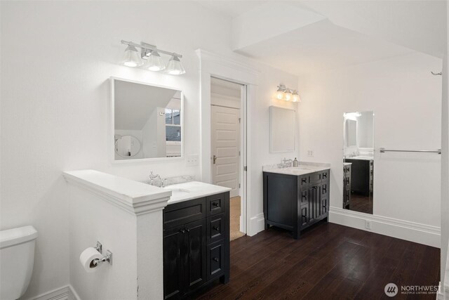bathroom featuring wood finished floors, toilet, two vanities, and baseboards