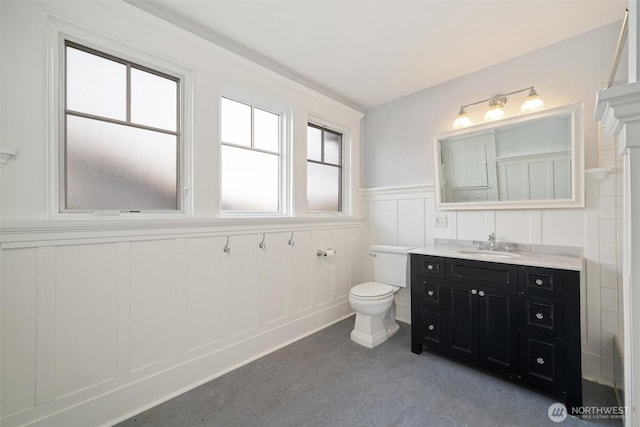 bathroom with a decorative wall, toilet, wainscoting, and vanity