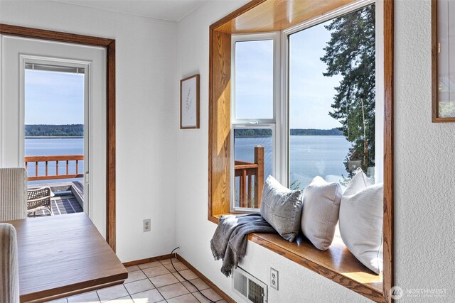 doorway with a water view, light tile patterned floors, and baseboards