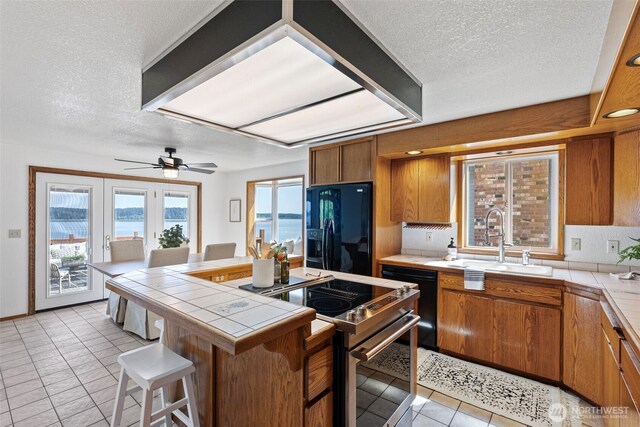 kitchen featuring tile countertops, stainless steel range with electric stovetop, a sink, black fridge with ice dispenser, and a textured ceiling