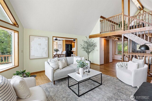 living room with high vaulted ceiling, healthy amount of natural light, stairway, wood finished floors, and baseboards