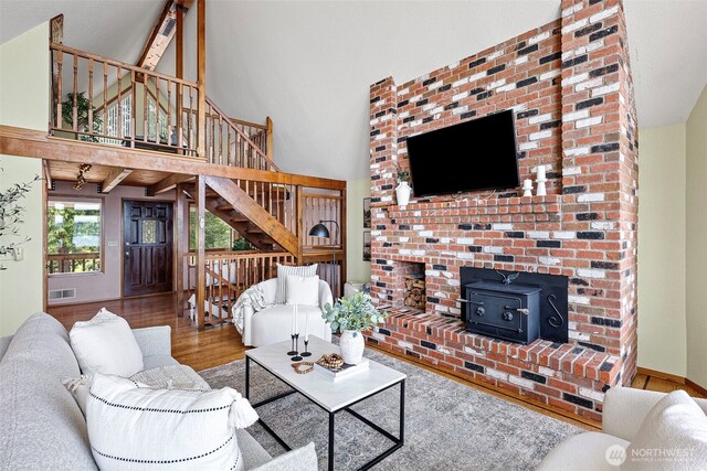 living room featuring a wood stove, wood finished floors, a towering ceiling, and stairs