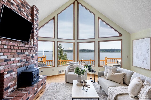 living room with a water view, vaulted ceiling, a wood stove, a textured ceiling, and wood finished floors